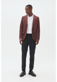 Burgunderfarbener Wildleder-Blazer mit Revers, kombiniert mit einem weißen Hemd, schwarzen Hosen und schwarzen Slippern. Glatte Textur und taillierter Schnitt.
