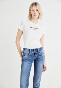 T-shirt en coton blanc avec le logo noir "Pepe Jeans London", associé à un jean en denim bleu clair avec fermeture à double bouton et décoloration subtile.