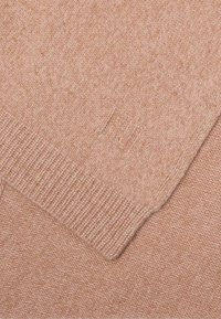 Lichtroze gebreide trui met een gestructureerd patroon, geribde manchetten en een subtiele logo-detail op de stof. Zachte en gladde textuur.