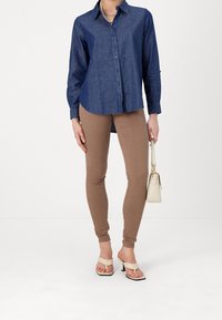 Jeansskjorta med knappar, mörkblå; beiga snäva byxor; vita klacksandaler; liten vit handväska; släta texturer; avslappnad outfit.