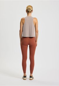 Top senza maniche di un grigio chiaro abbinato a leggings di colore ruggine. Il tessuto appare morbido, con una vestibilità rilassata e dettagli minimi.