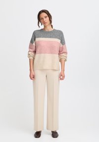 Maglione testurizzato con righe orizzontali grigie, rosa e crema, abbinato a pantaloni larghi beige e scarpe marroni scure.