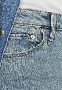 Svijetloplave traperice s vidljivim džepom, bakrenim šavovima i detaljem kopče, koje prikazuju glatku teksturu i klasičan dizajn.