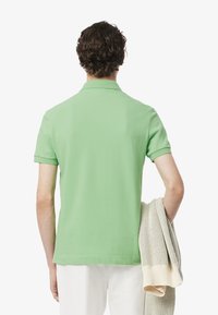 Grön polo med spetsig krage, korta ärmar och rak nederkant. Modellen håller en ljus krämfärgad stickad tröja.