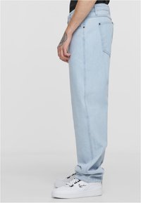 Heledad sinine teksad, sirgete lõikega, millel on tagakotid ja sile tekstuur. Kombineeritud valgete spordijalatsitega.