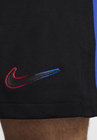 Nike shorts i sort mesh med blå og sorte accenter. Har et skinende Swoosh-logo omkranset af rød og blå, som viser en distinkt tekstur.