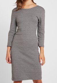 Klänning med hundtandsmönster, tillverkad av ett texturerat tyg, med båtformad halsringning och trekvartsärmar, skräddarsydd för en figurnära silhuett.