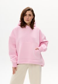 Rosa übergroßer Hoodie aus weichem Baumwollmischgewebe mit großer Fronttasche, Kapuze mit Kordelzug und gerippten Bündchen. Glatte Textur.