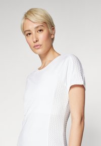 White athletic t-shirt with short sleeves, featuring a textured panel on the side, round neck, and smooth fabric finish.