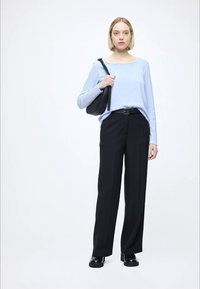 Top azul claro de manga comprida, calças largas pretas, cinto preto e mala preta. A modelo usa sapatos pretos com sola grossa. Fundo neutro.