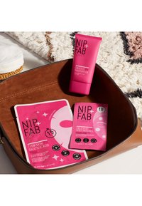 NIP + FAB Purify crème hydratante salicylique rose, masque de soin pour peau d'ado et patchs ciblés dans un sac marron ; textures lisses, couleurs vives, étiquetage clair.