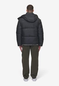 Black puffer jacket with a hood, featuring horizontal stitching, a relaxed fit, and a smooth texture. Paired with olive cargo pants and sneakers.