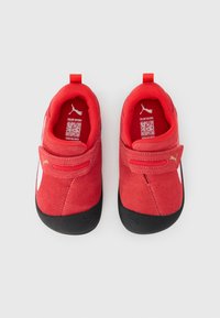 Czerwone zamszowe sneakersy z czarnymi gumowymi podeszwami, z rzepem, teksturowanymi akcentami i białym logo marki z boku.