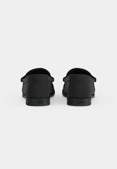 Ζευγάρι μαύρα loafers χωρίς κορδόνια, εμφανισμένα από πίσω σε απλό φωτεινό φόντο.