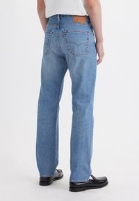 Vaqueros de mezclilla azul claro con un diseño de pierna recta, que cuentan con dos bolsillos traseros y una etiqueta de cuero marrón en la cintura.