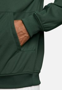Felpa verde con orlo e polsini a coste, dotata di tasca laterale. Il materiale appare liscio con una finitura opaca.