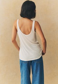 Débardeur blanc à côtes avec un dos en U, associé à un jean en denim bleu ample. Le tissu semble doux avec une texture subtile.