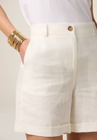 Linnen shorts in gebroken wit, met een knoopsluiting, zijzakken en opgerolde mouwen. Soepele textuur met een natuurlijke, lichte uitstraling.