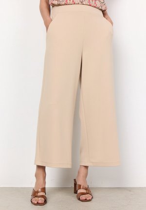 Beige wide-leg trousers with a smooth texture, side pockets, and a fitted waistband, paired with brown heeled sandals.