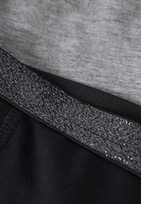 Μαύρη αθλητική ζώνη μέσης με υφή γκρι μοτίβου, τοποθετημένη πάνω από λείο γκρι ύφασμα. Διαθέτει λαμπερή, λαμπυρίζουσα λεπτομέρεια στη ζώνη μέσης.