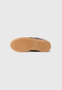Suela de zapato marrón con patrones de bandas, círculos y panal en un fondo claro.