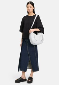 Sac à épaule blanc avec des coutures noires, associé à une chemise surdimensionnée noire, une jupe en denim taille haute et des sandales à plateforme noires.