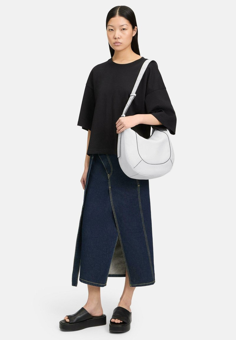 Sac à épaule blanc avec des coutures noires, associé à une chemise surdimensionnée noire, une jupe en denim taille haute et des sandales à plateforme noires.