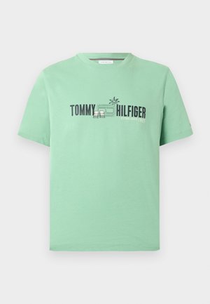 Mint πράσινο T-shirt Tommy Hilfiger με μαύρο κείμενο και μικρό σχέδιο με φοινικόδεντρο και καρέκλες πάνω από ένα παράθυρο.