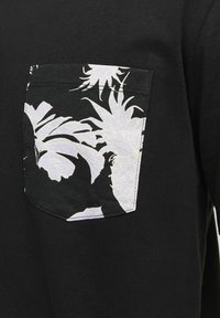 Sort t-shirt med en hvid og grå mønstret lomme med tropiske blade og ananasdesignet. Lavet af bomuldsmateriale, afslappet pasform.