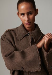 Brown corduroy jacket with large collar and frayed edges, featuring a button closure and wide sleeves, highlighting a textured surface.