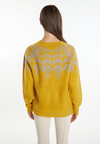 Maglione giallo con una texture morbida, caratterizzato da un motivo botanico grigio sulla parte posteriore. Maniche lunghe e scollatura rotonda completano il design.