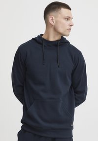 Felpa con cappuccio di colore blu navy realizzata in tessuto morbido, dotata di tasca a marsupio, cappuccio regolabile con lacci e polsini a coste.