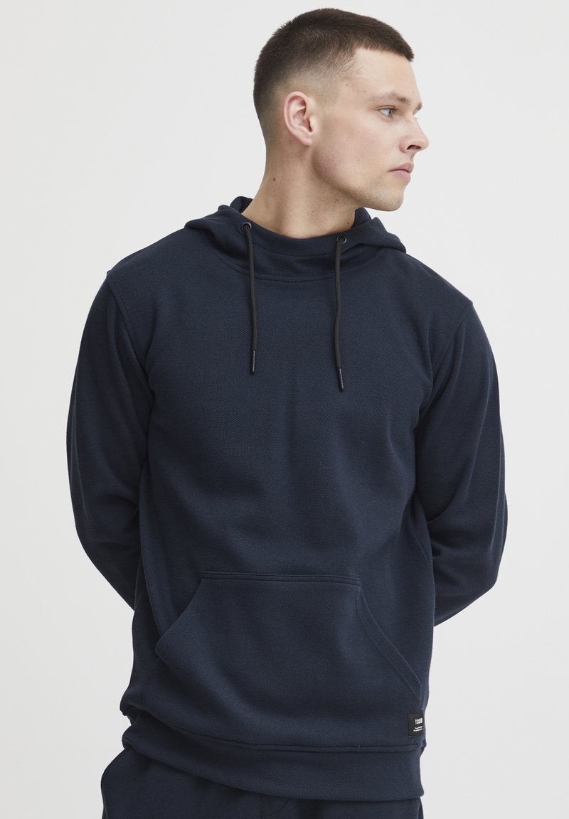 Felpa con cappuccio di colore blu navy realizzata in tessuto morbido, dotata di tasca a marsupio, cappuccio regolabile con lacci e polsini a coste.