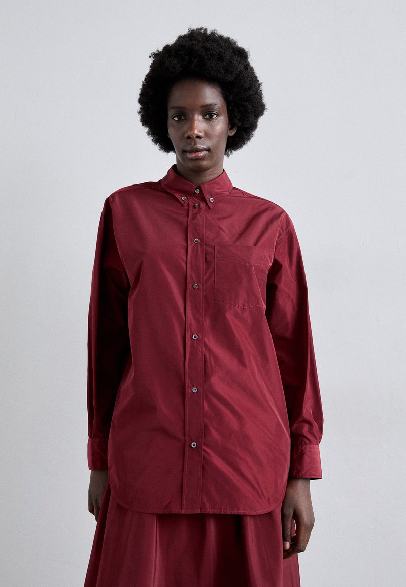 Crimson button-up shirt with long sleeves, a chest pocket, and a straight cut. Made from smooth, lightweight fabric. Silver-tone buttons.