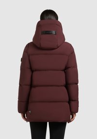 Bordó pufi dzseki magas kapucnival, steppelt kialakítással, sima textúrával és fekete logóval a hátsó részen. Enyhén lejjebb nyúló hátsó rész jellemzi.