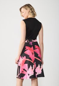 Robe noire avec un haut ajusté et une jupe évasée. La jupe présente un motif floral rose vif avec des accents noirs et une taille unie.