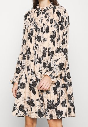 Robe fleurie en tissu pêche doux avec des motifs de roses noires, présentant un col rufflé et des manches longues avec des poignets froncés. Coupe décontractée.