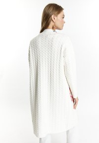 Cardigan bianco lavorato a maglia con motivo a treccia, maniche lunghe e vestibilità comoda. Presenta un dettaglio decorativo colorato visibile di lato.