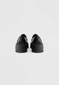 Black leather platform shoes with a chunky sole and rounded toe. Smooth texture with minimal stitching detail. Back view shows a sleek design.