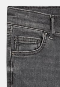 Grå denim jeans med en glatt tekstur, med en frontlomme og kontraststing. Inkluderer detalj med metallrivet på lommen.