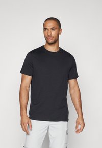 Schwarzes T-Shirt mit kurzen Ärmeln aus weichem Material, mit klassischem Rundhalsausschnitt und glatter Textur, getragen mit hellen Cargo-Shorts.