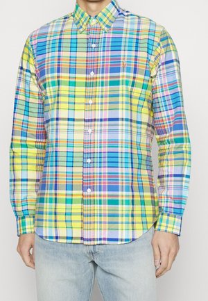 Mężczyzna noszący koszulę z długim rękawem w wielokolorową kratę i jasnoniebieskie dżinsy.