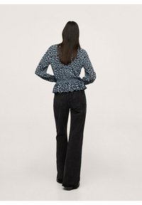 Blouse bleu foncé à motif floral avec ourlet bas smocké en forme de peplum, associée à un jean noir à jambes larges. Détail visible au dos et manches longues.