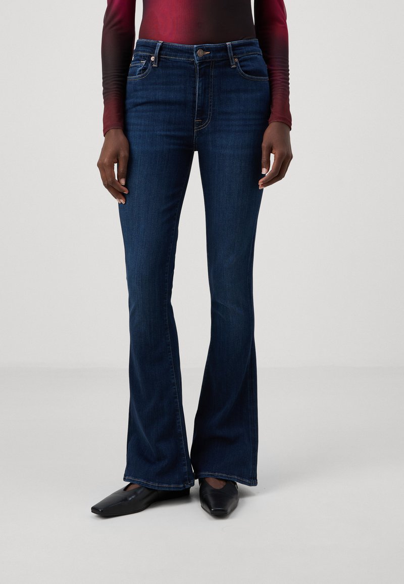 Blugi evazați de culoare albastru închis, din denim, având o talie medie, cusături subtile și o textură netedă. Completați cu pantofi negri cu vârf ascuțit.