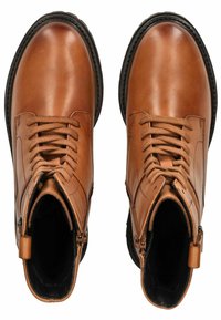 Bottes de cheville en cuir tan avec des embouts arrondis, un design à lacets, des zips sur les côtés et des semelles en caoutchouc noir. Texture lisse avec des détails de couture minimalistes.