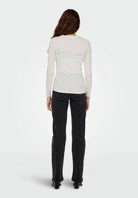 Camicia bianca a maniche lunghe con un design aderente, texture morbida e orlo curvo, abbinata a pantaloni a vita alta neri svasati e tacchi grossi.