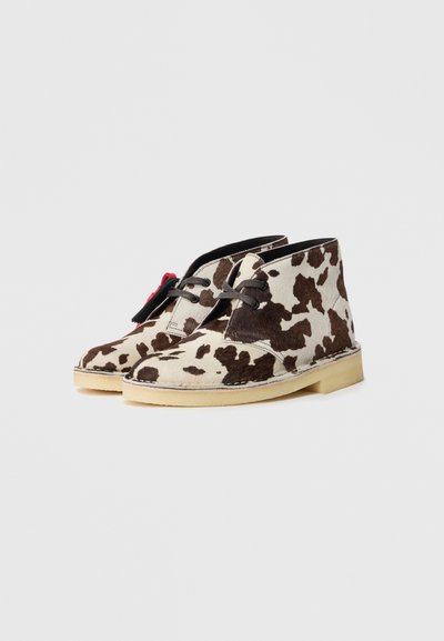 Chukka boots w czarno-beżowy wzór w krowie cętki, z wiązaniem na sznurówki i kremową gumową podeszwą.