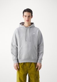 Grauer Hoodie aus Baumwoll-Mischgewebe, mit einer Fronttasche, Kordelzugkapuze und einem kleinen New Balance-Logo auf der Brust.
