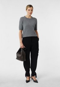 Szary sweter z krótkim rękawem, obcisłe czarne spodnie z wiązaniami przy kostkach oraz szare szpilki z wydłużonym noskiem. Modelka trzyma ciemnobrązową torebkę.