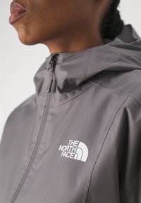 Szara kurtka na zamek z kapturem, z białym logo na lewej piersi. Gładki, lekki materiał z widocznymi szczegółami szwów.